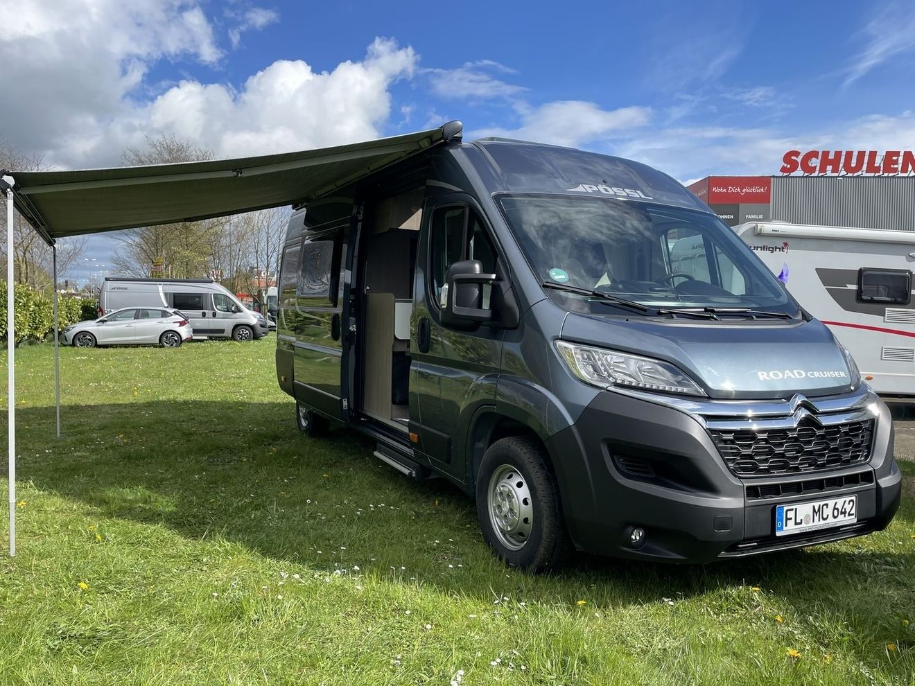 Ein Wohnmobil, das auf einer Wiese neben einem bunten Zelt unter strahlend blauem Himmel geparkt ist