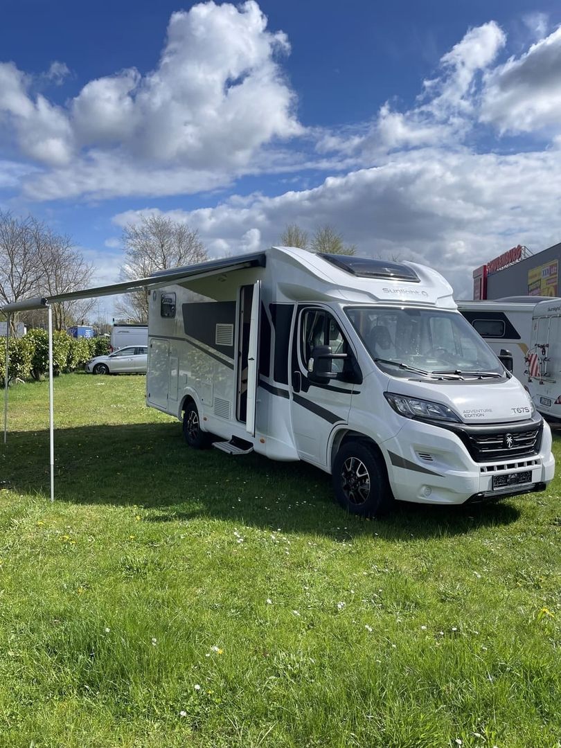 Wohnmobil auf einer Rasenfläche geparkt, mit ausgefahrener Markise