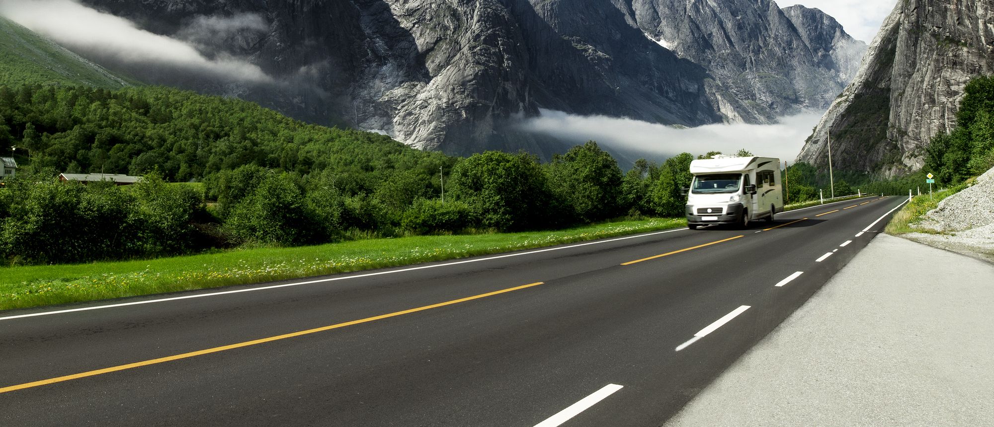 Ein Wohnmobil fährt auf einer malerischen Straße, umgeben von hoch aufragenden Bergen und üppigem Grün