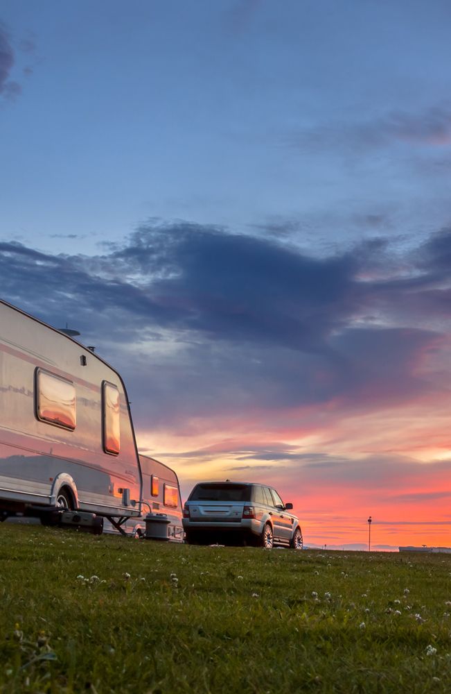 Wohnwagen und SUV, die bei Sonnenuntergang auf einer Wiese geparkt sind