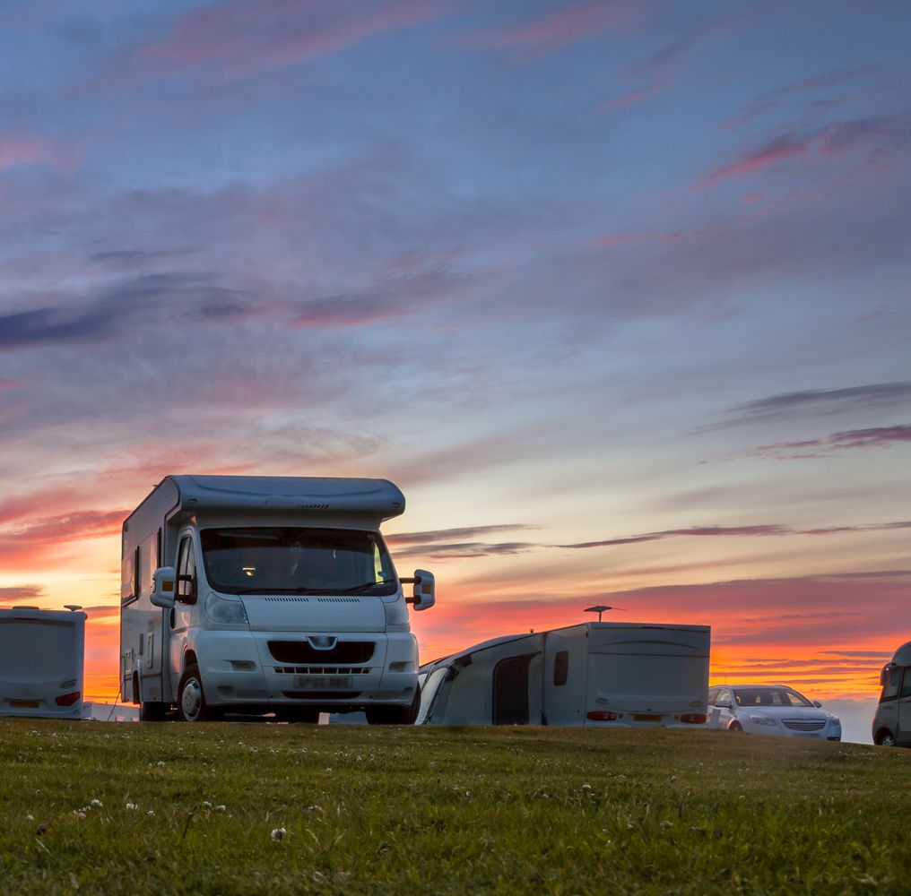 Ein Wohnmobil und ein SUV stehen auf grünem Gras unter einem strahlenden Sonnenuntergangshimmel